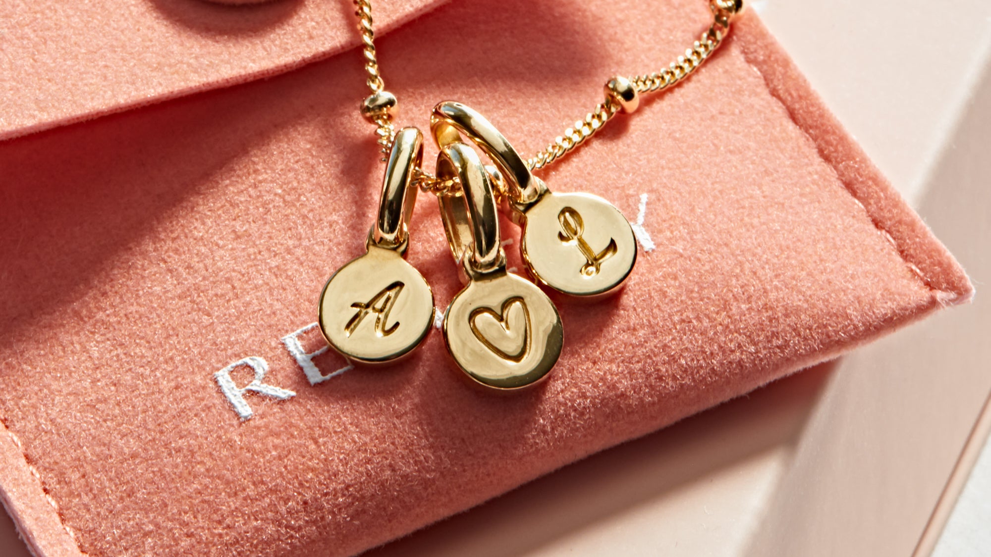Disk necklace with initial A, heart symbol, and initial L